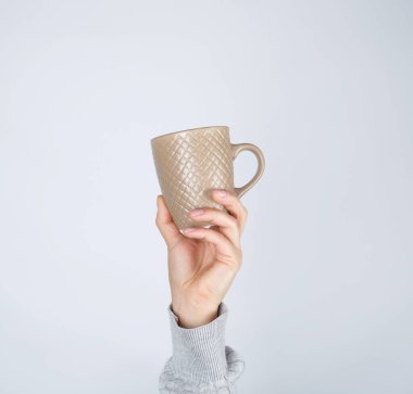 Kahverengi seramik bardak beyaz arka planda bir kadının elinde, el kaldırılır.