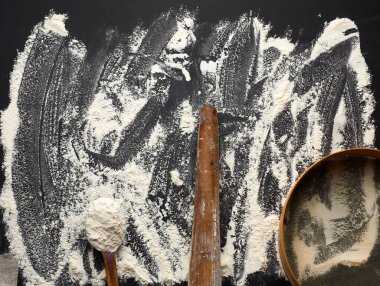 Siyah bir masaya saçılmış beyaz buğday unu ve çok eski kahverengi ahşap bir iğne, yuvarlak elek, üst manzara.