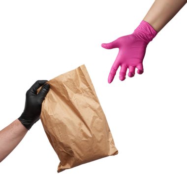 Siyah bir lateks eldiven içinde tam kahverengi bir paket ve pembe eldivenli bir kadın eli bir nesneye uzanıyor, çevrimiçi siparişlerin güvenli bir şekilde teslim edilmesi, beyaz arka plan