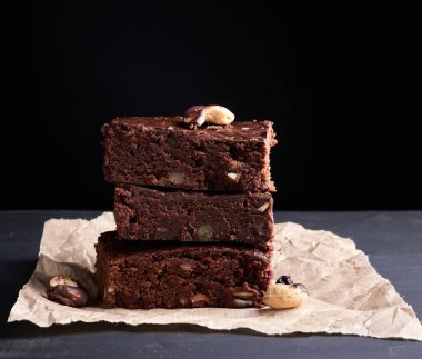 Ahşap yüzeyinde ceviz olan kare şeklinde çikolatalı kek yığını. Ev yapımı yemek. Çikolatalı pasta. Tatlı yemek, ev yapımı tatlı.