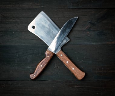 Kahverengi ahşap bir yüzeyde iki keskin bıçak bulunur. Mutfak eşyaları kesişir.