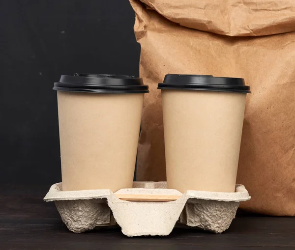 Kahverengi kağıt bardaklar, plastik kapaklı tepsi, ahşap masa, siyah arka plan, paket servis kapları.