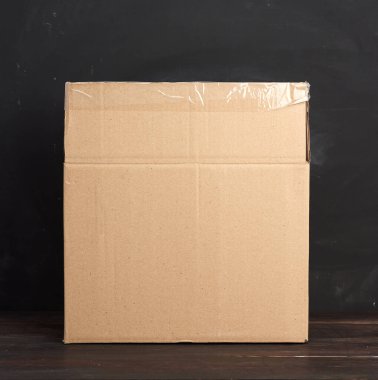 Kahverengi bir masanın üzerinde duran karton kutuyu aç, eşyaları taşıma ve paketleme konseptini kapat.