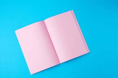Mavi arkaplan üzerinde boş pembe sayfaları olan açık bir defter, üst görünüm, düz uzanma