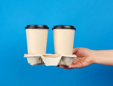 Tepside plastik kapaklı iki tane tek kullanımlık kahve bardağı, mavi arka planda tek kullanımlık masa takımı.