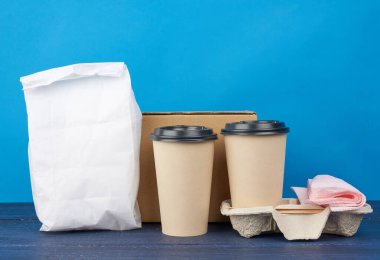 tamamen beyaz kağıt torba ve plastik kapaklı kahverengi tek kullanımlık bardaklar mavi ahşap bir masanın tepsisinde, paket servis kapları