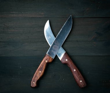 Kahverengi ahşap bir yüzeyde iki keskin bıçak bulunur. Mutfak eşyaları kesişir.