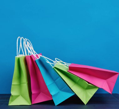Alışveriş için sapı ve mavi arka planda hediyeleri olan çok renkli kağıt poşetler.