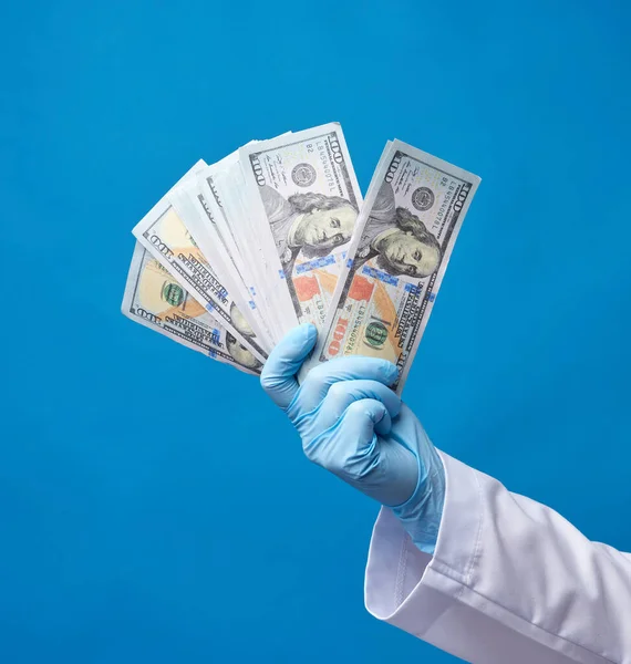 Doktor, mavi steril eldiven giyen beyaz önlüklü bir doktor elinde bir deste kağıt para, yolsuzlukla mücadele konsepti, rüşvet ve yapılan iş için ödeme tutuyor.