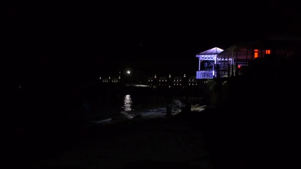 Restaurante en la playa por la noche cuando la luna camino iluminación en las olas — Vídeo de stock