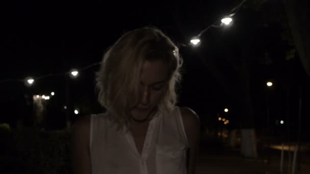 Блондинка, одягнена тільки в сорочку, йде сама вночі на вулиці освітлення — стокове відео
