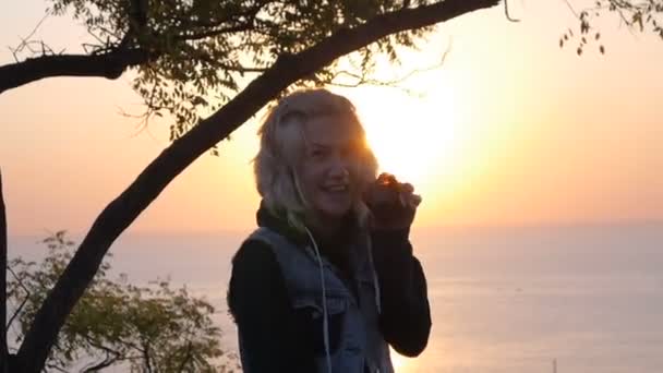 Sorriso menina com celular desfrutar momento em que o nascer do sol refletindo sobre o mar — Vídeo de Stock
