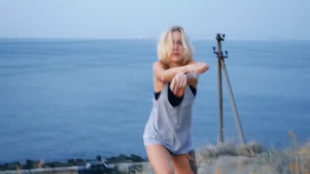 Hermosa chica rubia baila en la playa al amanecer y cerca de la montaña — Vídeos de Stock