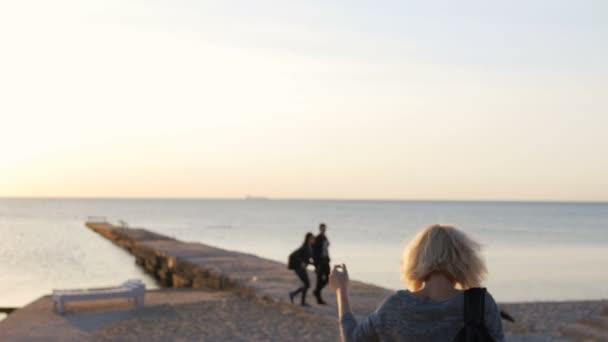 Schöne Mädchen spaziert mit ihrer bunten Tasche lächelnd am Strand bei Sonnenaufgang — Stockvideo