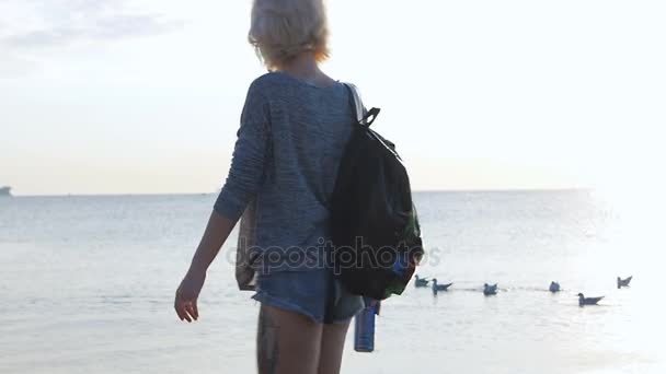 Hermosa chica camina con su colorida bolsa sonriendo cerca de la playa al amanecer — Vídeos de Stock