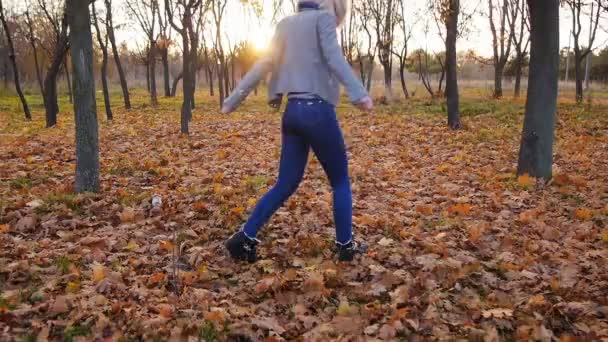 Jeune femme bonheur dansant parmi les feuilles colorées d'automne au coucher du soleil 
