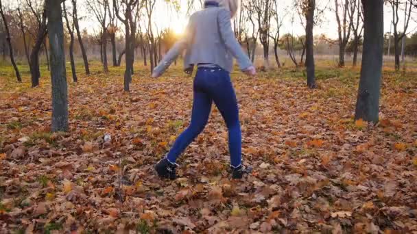 Jonge vrouw geluk dansen onder de kleurrijke herfst bladeren in de zonsondergang — Stockvideo
