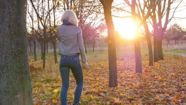 Jeune femme bonheur dansant parmi les feuilles colorées d'automne au coucher du soleil 