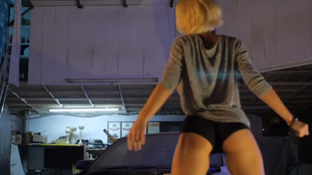 Blondes Mädchen tanzt in Garage in der Nähe der Reifen und Autos super sexy — Stockvideo
