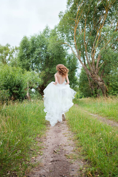 Portrait of young pretty woman (bride) in white wedding dress outdoors running away