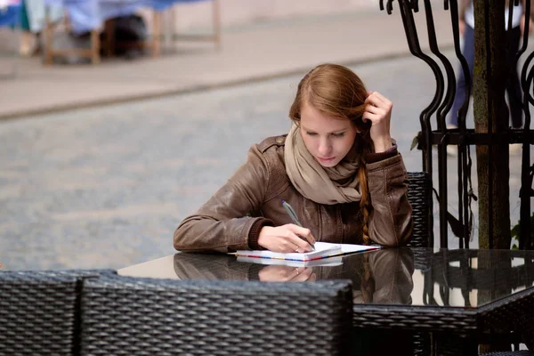Ruiva menina sentada na cidade rua café e escrita ou desenho — Fotografia de Stock