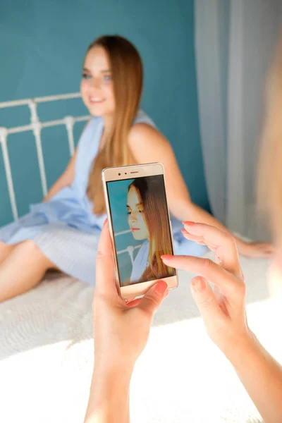 taking photo on phone of young pretty girl sitting on bed
