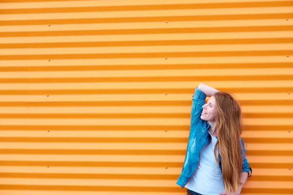 Рыжая девушка в джинсовой рубашке возле оранжевой стены — стоковое фото