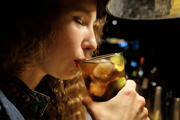 redhead girl sitting in bar (pub) drinking icy cocktail alone