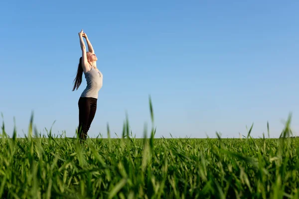 girl stretching herself in green field with blue sky background