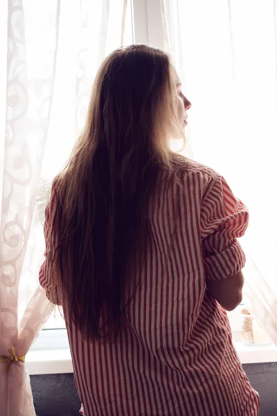Roodharige meisje op zoek in het venster in de ochtend — Stockfoto