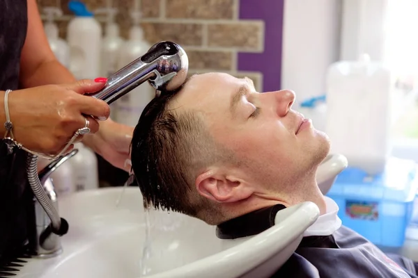 Peluquero lavar el cabello a un hombre joven, que tiene placer y s — Foto de Stock