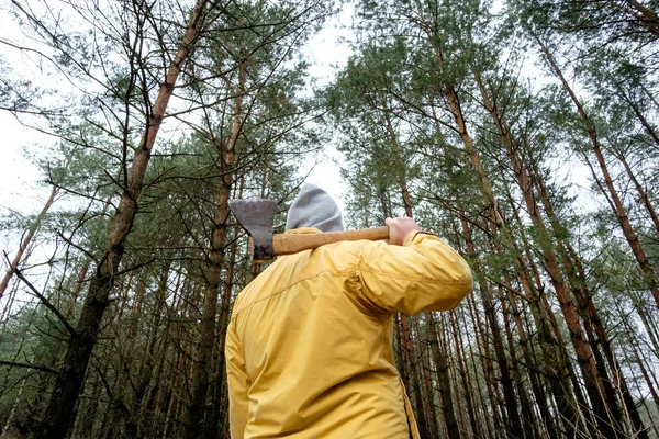 Uomo in giacca gialla nella foresta con ascia — Foto Stock