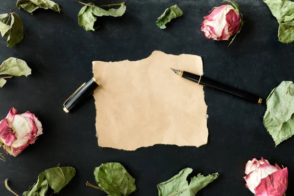 Pedaço de papel com caneta estilete e rosas secas e folhas em bla — Fotografia de Stock