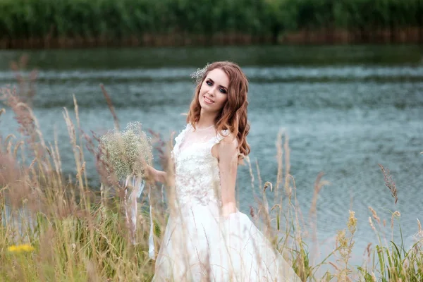 Portret van de bruid in witte bruiloft jurk met boeket in de buurt van lake — Stockfoto