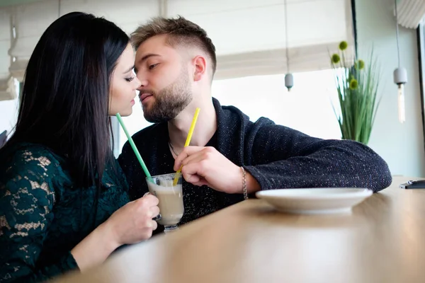 Jovem casal sentado no café, bebendo capuccino e beijando eac — Fotografia de Stock