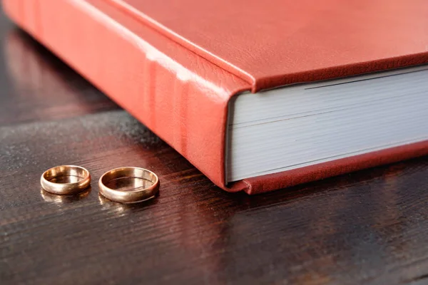 Brown wedding album with two wedding rings lie on brown wooden b