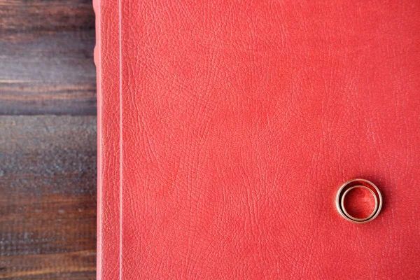 Red wedding album with two wedding rings on surface lie on brown