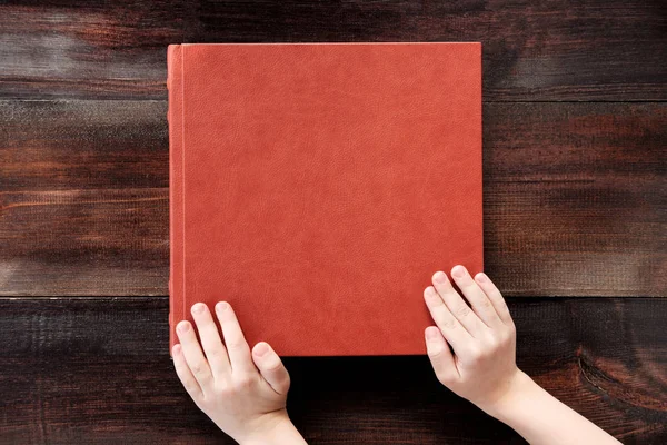 Kind hält Hand an braunem lederbezogenem Hochzeitsalbum oder Buch — Stockfoto