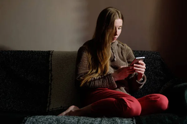 Rødhåret ingefærjente i hettegenser leser på smarttelefon, sitter – stockfoto