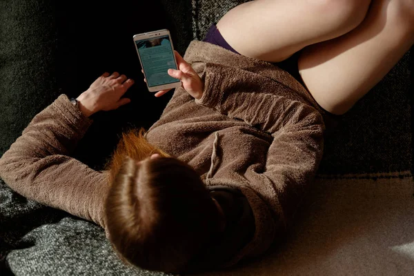 Gember roodharige meisje in hoodie app op smartphone, sittin kijken — Stockfoto