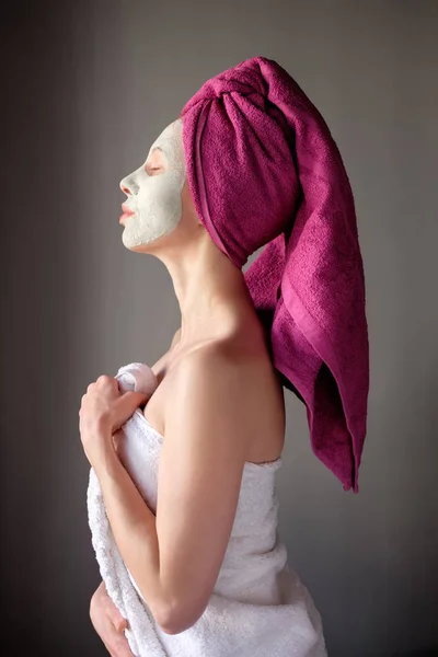 Mujer en spa con toalla púrpura en la cabeza y máscara de arcilla en la cara. Wo. — Foto de Stock