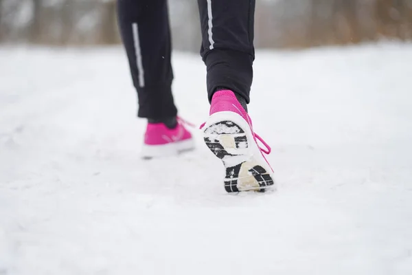 Female feet in pink sneakers while jogging in winter forest.
