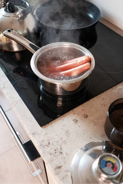Киплячі ковбаски на фритюрі на кухні — стокове фото