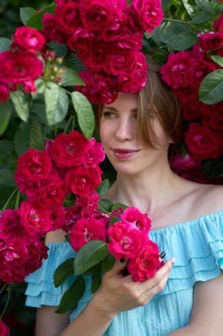 Bahar. Bahçede çiçek açan güller kokan zarif mavi bir elbise giyen güzel kızıl saçlı genç bir kadının portresi. Açık hava..                               