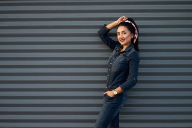 Modern bahar koleksiyonu. Uzun esmer saçlı, kırmızı dudaklı, modern kot pantolon giyen, gri kentsel arka planda poz veren şık bir kadın..                               