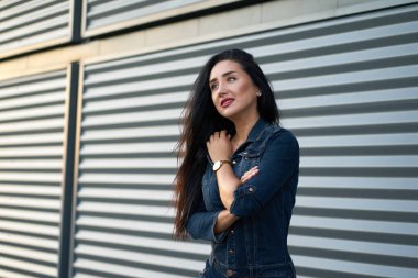 Yeni moda koleksiyon. Gri şehir arka planında modern kot pantolon giyen, uzun saçlı ve kırmızı dudaklı güzel, modaya uygun esmer bir kız portresi..                               