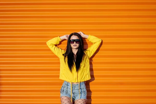 아가씨 유행하는 노란색 재킷을 반바지를 주황색 배경에 선글라스를 — 스톡 사진