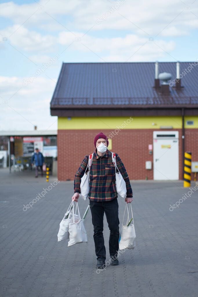 Caucasian man wearing medical mask carryin bags with food after shopping during outbreak
