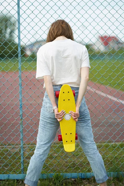 Rødhåret Hvid Pige Med Skateboard Nær Hegn Stående Baglæns - Stock-foto
