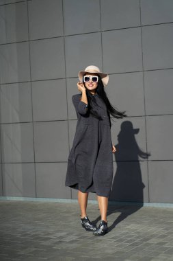 Bahar modası koleksiyonu. Şık gri elbiseler ve şık şapkalar giyen güzel esmer kız. Güneşli bir günde gri duvarda poz veren modaya uygun kıyafetler..                             